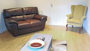 A living room with a brown leather sofa, a yellow armchair, a coffee table with a bowl and remote, and a white door in the background. - 1 bedroom accommodation in Tenby (Tenby)