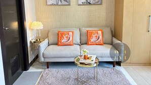 En moderne stue med en grå sofa, to orange puder, et rundt sofabord med et magasin, og en dekorativ lampe.