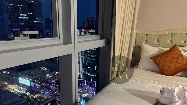 Et hotelværelse med et stort vindue der giver udsigt over byen, en seng med hvide sengetøj, en betrukken gavl og en enkelt brun pude.