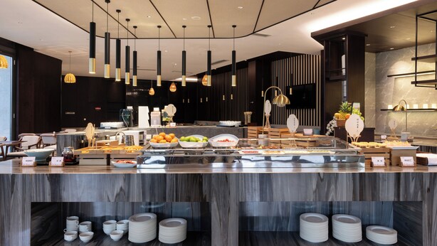 Un moderno bufé hotelero con una variedad de alimentos, una estación de café y platos y vasos ordenados.