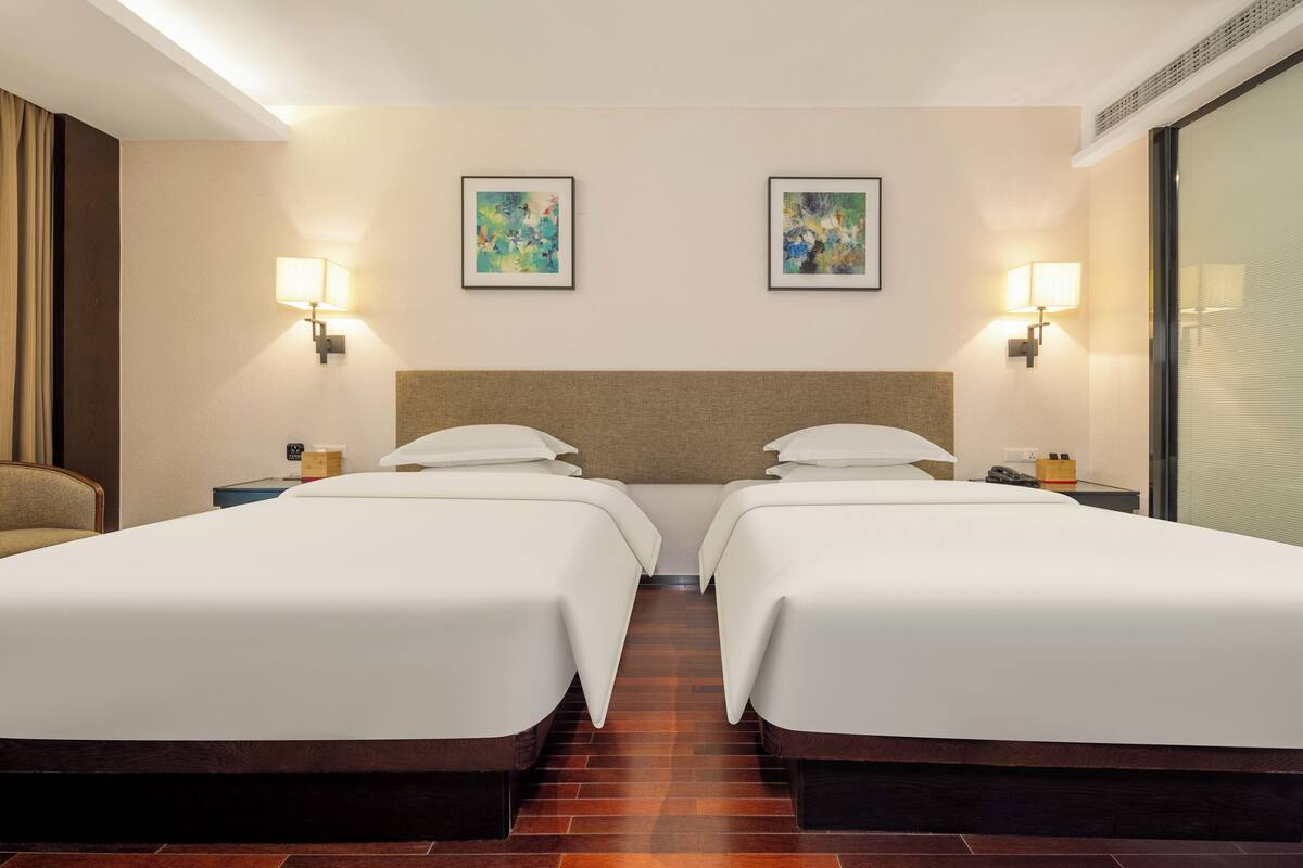 Habitación de hotel con dos camas, cabeceros, lámparas de pared y obras de arte en las paredes.
