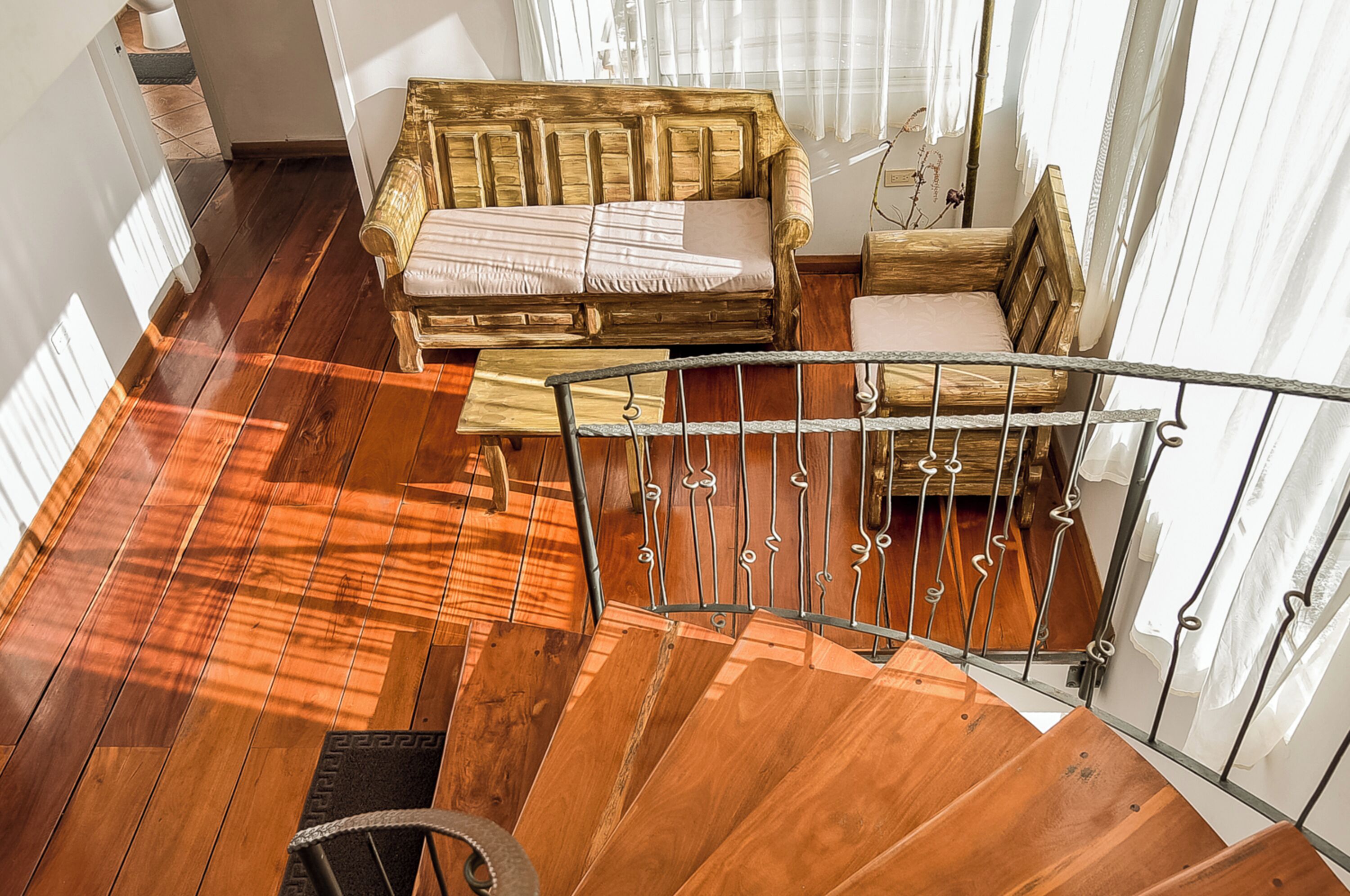 A wooden staircase with a metal railing leading to a room with a wooden sofa and a bed.