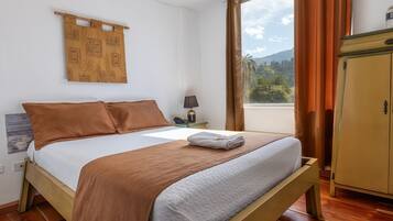 Een net opgemaakt bed met een bruin-witte dekbedovertrek, een houten hoofdbord en een raam met gordijnen.
