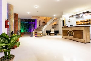 Un vestíbulo amplio con una escalera, una recepción y plantas en macetas.