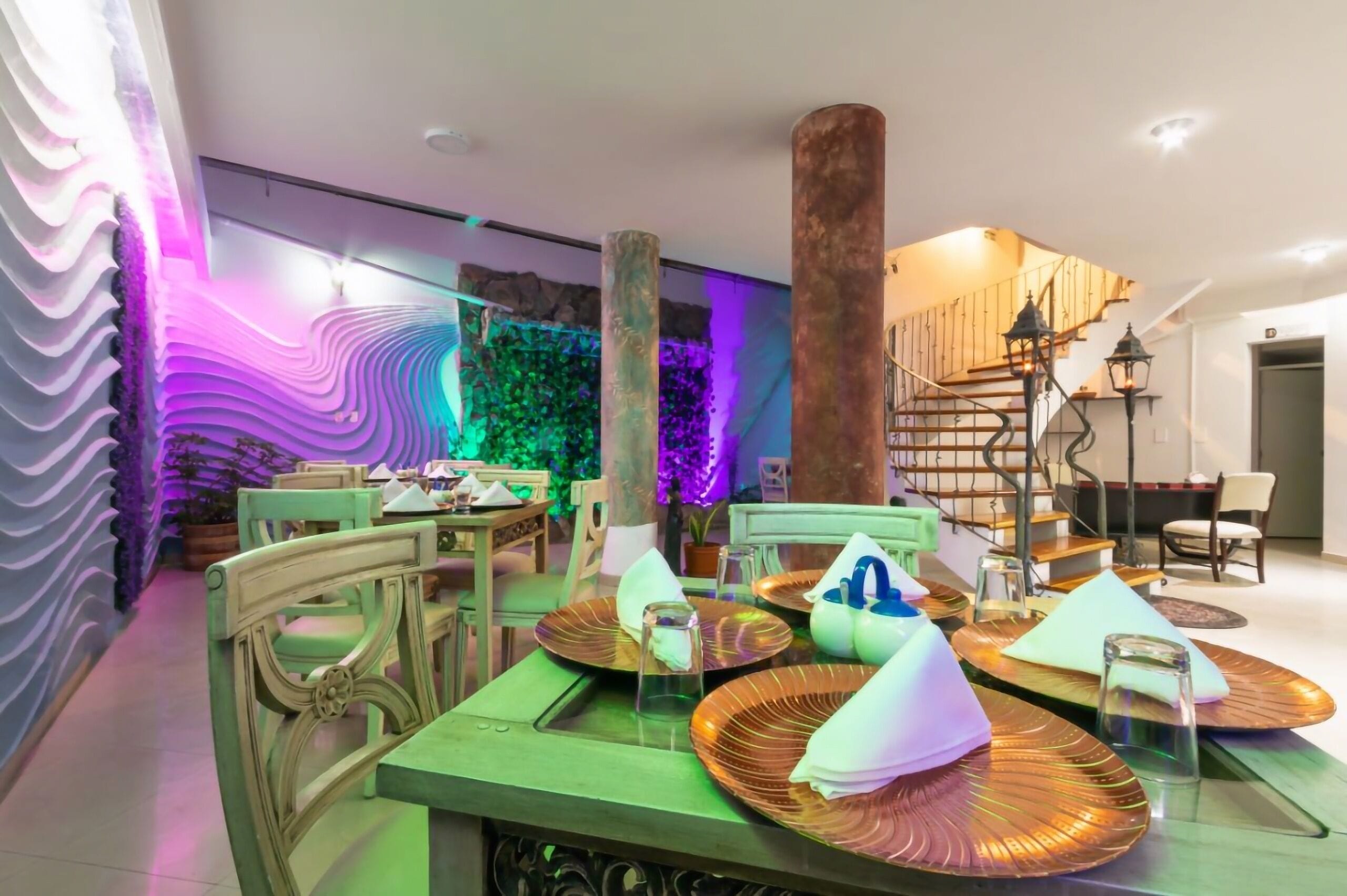 A dining area with green chairs and tables, a staircase, and a wall with a textured pattern.