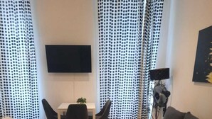 Ein modernes Wohnzimmer mit einer Couch, einem runden Couchtisch, einem Esstisch mit Stühlen und einem an der Wand montierten Fernseher.