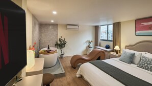 A modern hotel room with a bed, a desk, a chair, a small table with a lamp, a potted plant, and a large window. - Secret Garden Phan Xich Long (Ho Chi Minh City)