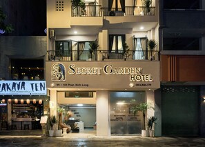 Das Äußere des Secret Garden Hotels, mit einer modernen Fassade, einem gut sichtbaren Eingang und einem Schild mit dem Namen und der Adresse des Hotels.