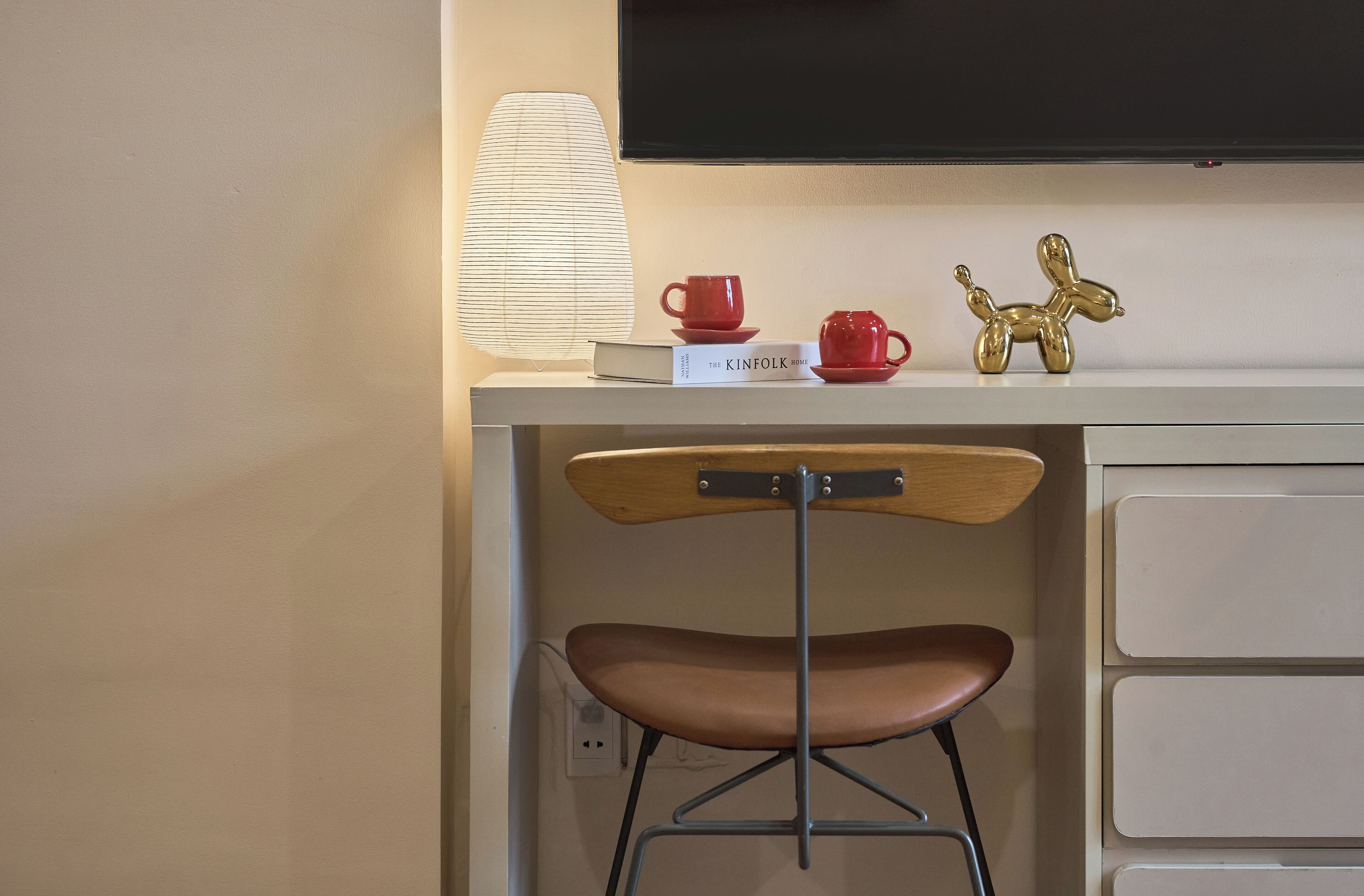 A desk with a lamp, a book titled 'The Kinfolk Home', a red cup, a red saucer, and a gold balsa wood sculpture.