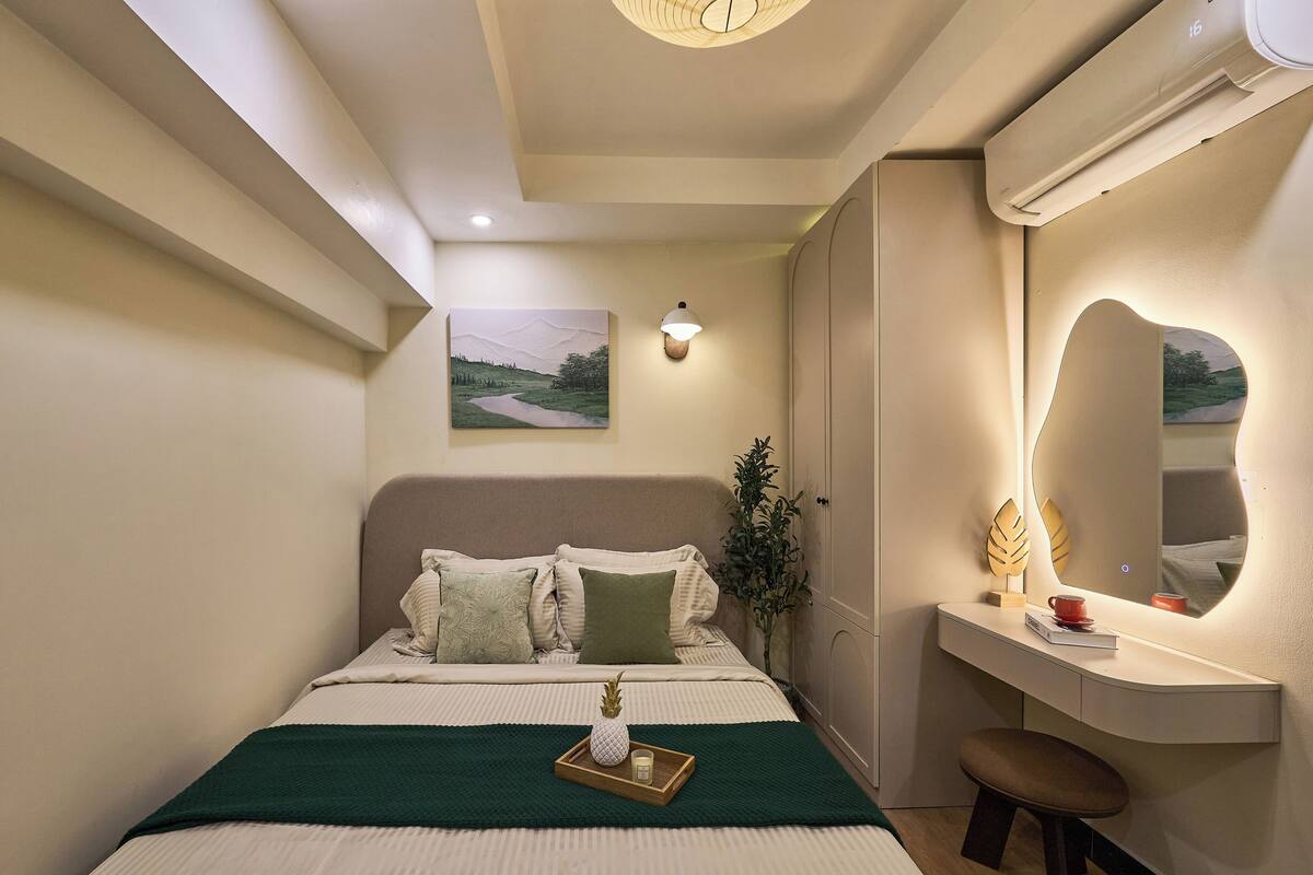 A bedroom with a bed, bedside table, mirror, and artwork on the wall.