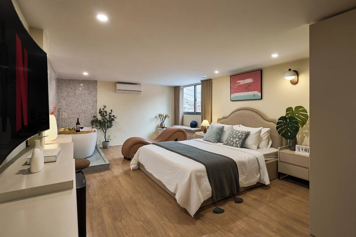 A modern bedroom with a large bed, bedside tables, a vanity, and a television.