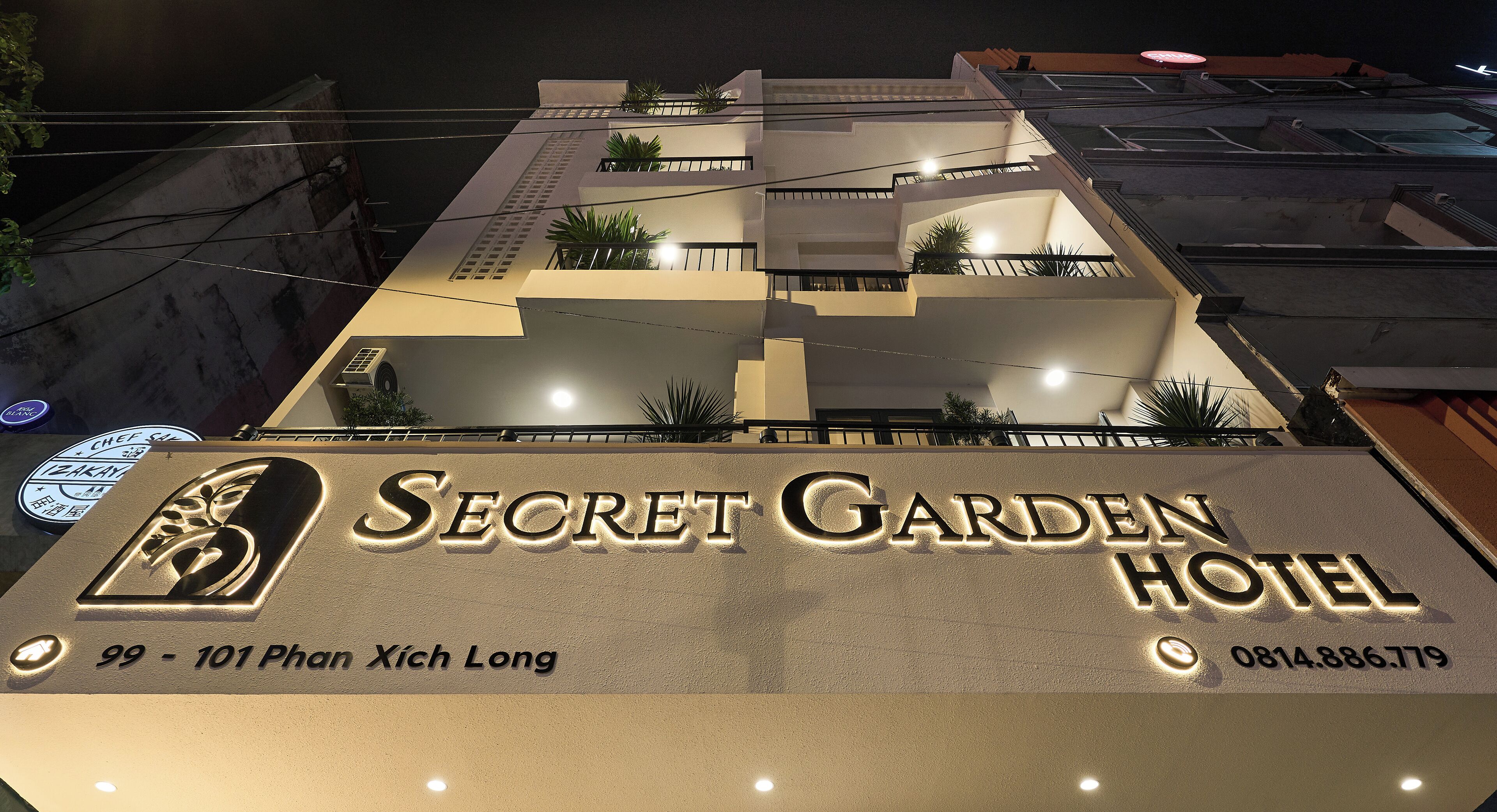 The exterior of the Secret Garden Hotel with illuminated signage, including the address and contact number.