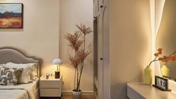 A neatly arranged bedroom with a bed, bedside table, lamp, potted plant, and a mirror reflecting the room.