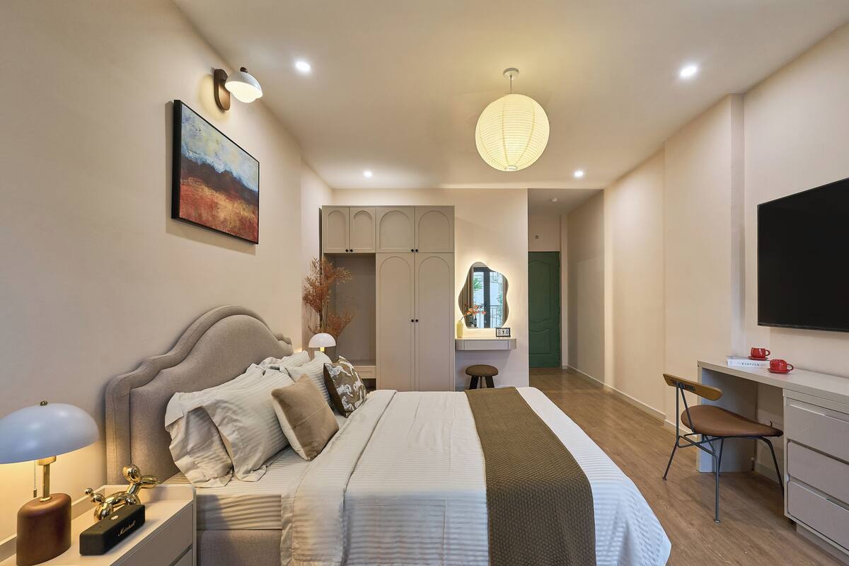 A modern bedroom with a bed, bedside table, lamp, and a desk with a chair.