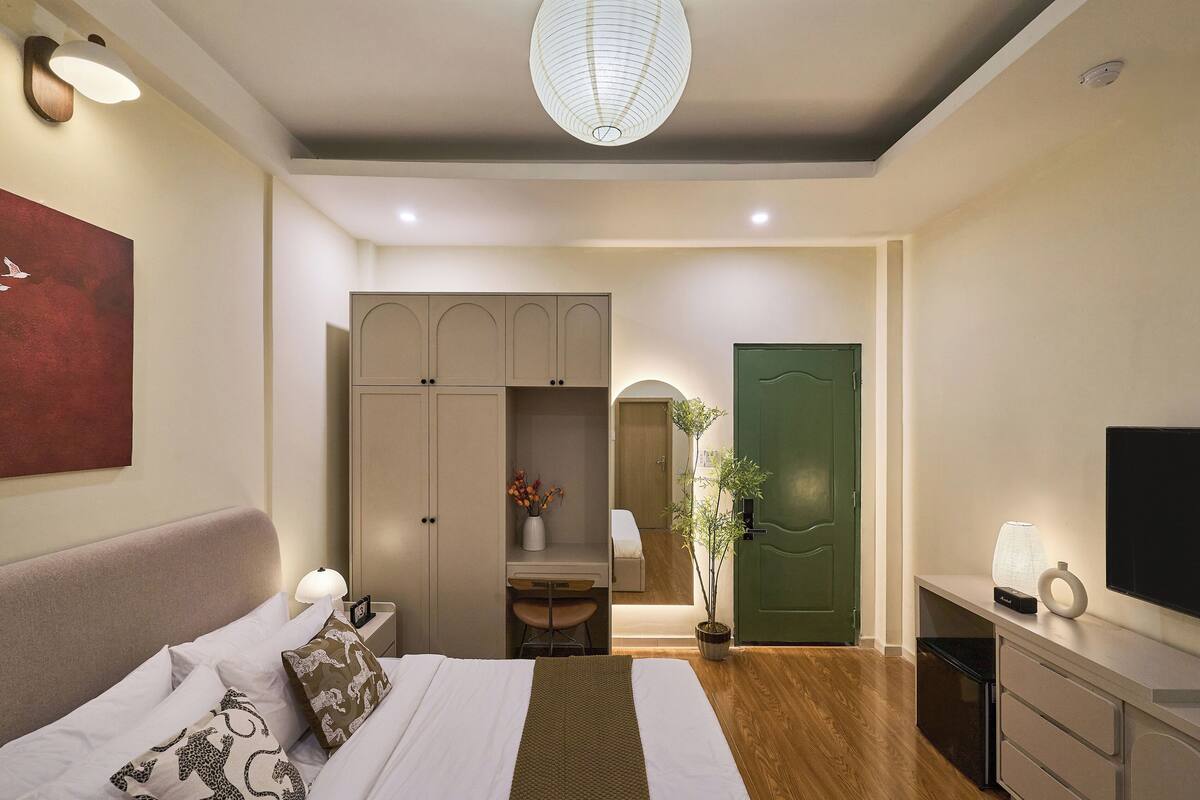 A modern bedroom with a bed, bedside table, lamp, wardrobe, mirror, green door, and a TV on a dresser.
