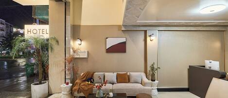 A hotel lobby with a reception desk, a sofa, a coffee table, and a potted plant.
