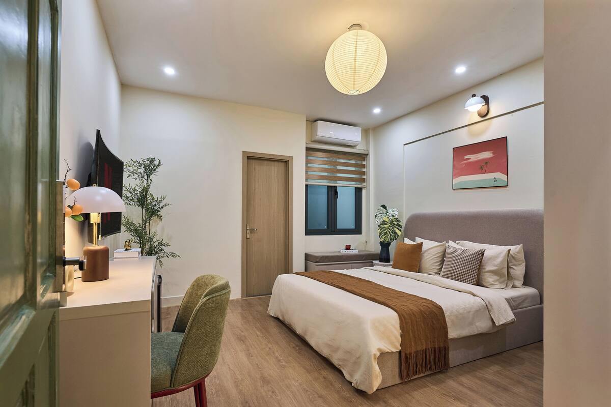 A modern bedroom with a bed, bedside table, lamp, chair, and a wall-mounted air conditioner.