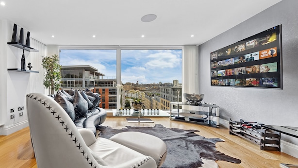 Ein modernes Wohnzimmer mit einer Ledersofa, einer großen TV-Wandgestaltung und Blick auf die Stadt.