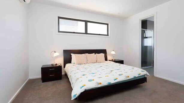 A bedroom with a bed, two bedside tables, a window, and a door leading to a bathroom.