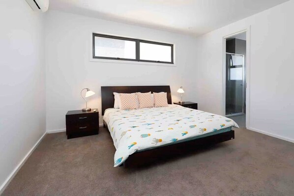 Un dormitorio con una cama, dos mesitas de noche, una ventana y una puerta que da a un baño.