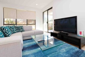 Una sala de estar moderna con un sofá, una mesa de centro de vidrio, un televisor de pantalla plana y un gran ventanal corredero.