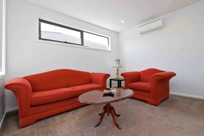 Una habitación pequeña y moderna con dos sofás rojos, una mesa de centro redonda y una ventana con vistas a edificios.