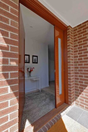 Un pasillo con pared de ladrillo, una consola blanca con un florero y una puerta que da a otra habitación.