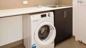 A compact hotel laundry room with a front-loading washing machine, a sink, and dark wooden cabinets.