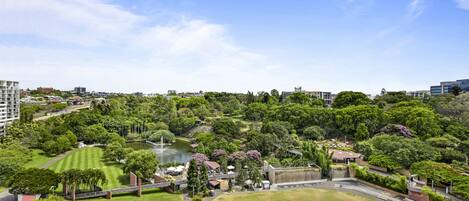 A park with a pond, walking paths, and various buildings in the background.