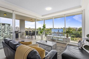 Una sala de estar moderna con un gran ventanal corredizo que da a un espacio exterior, un conjunto de sofás, una mesa de centro y vistas de la ciudad.