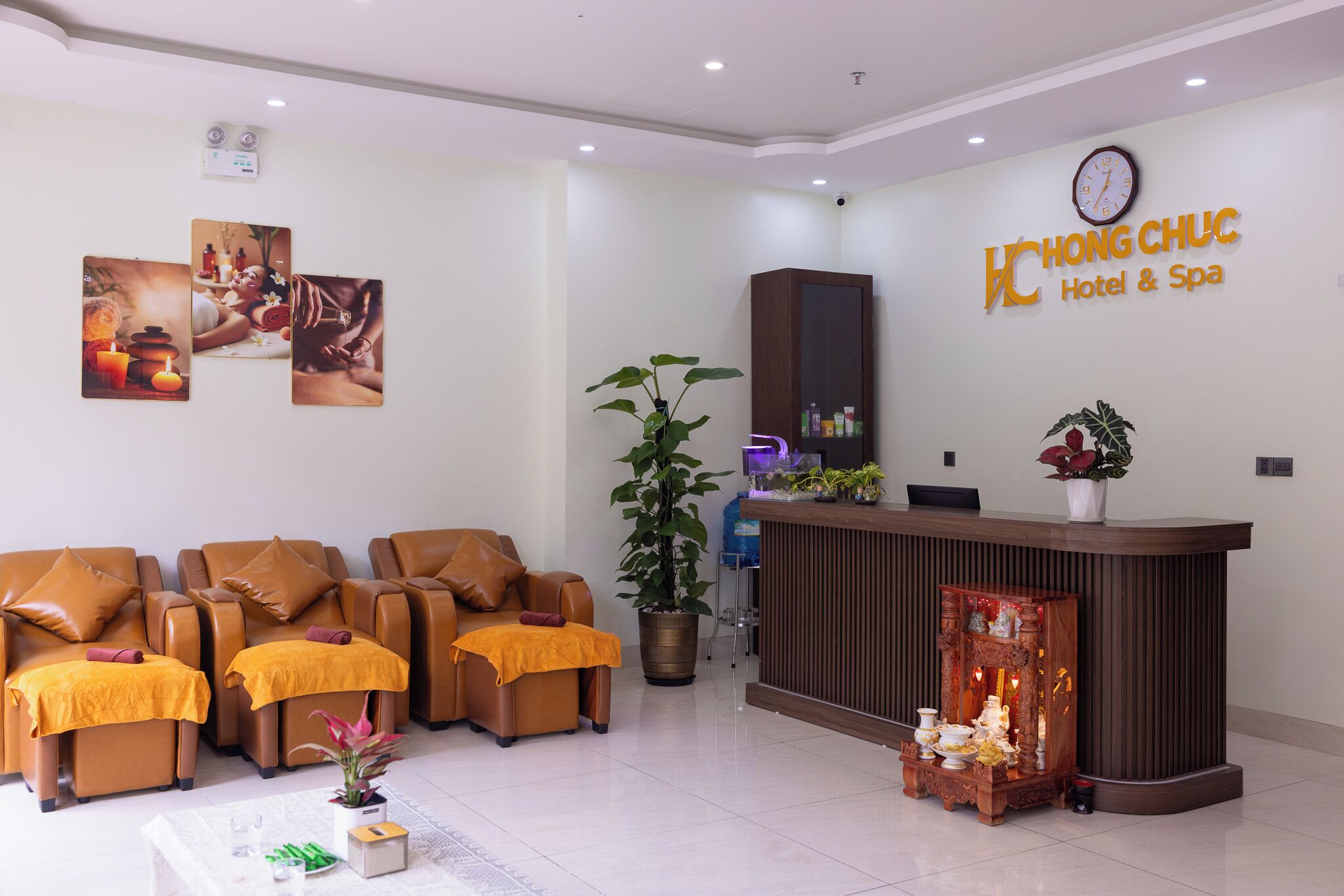 A hotel reception area with a reception desk, seating area with massage chairs, and wall-mounted artwork.