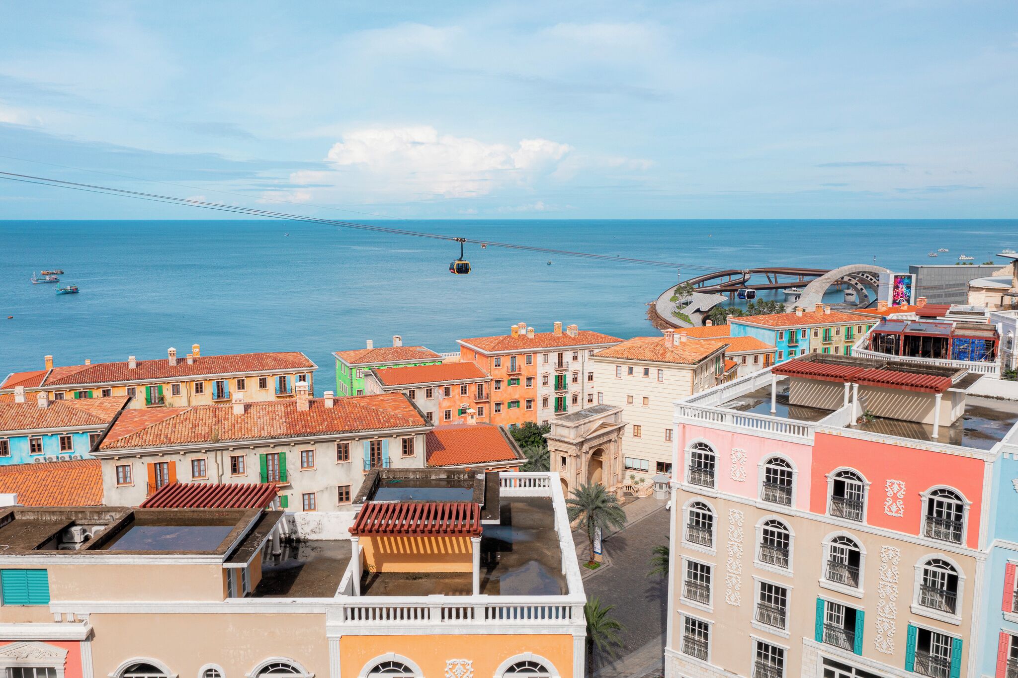 A coastal cityscape with colorful buildings, a cable car, and a clear view of the sea.
