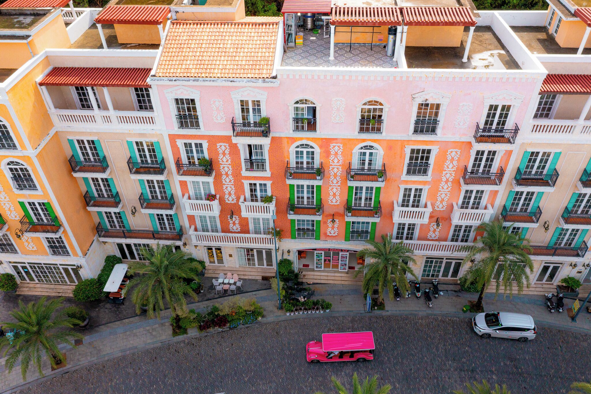 A multi-story building with balconies, a central courtyard, and palm trees.