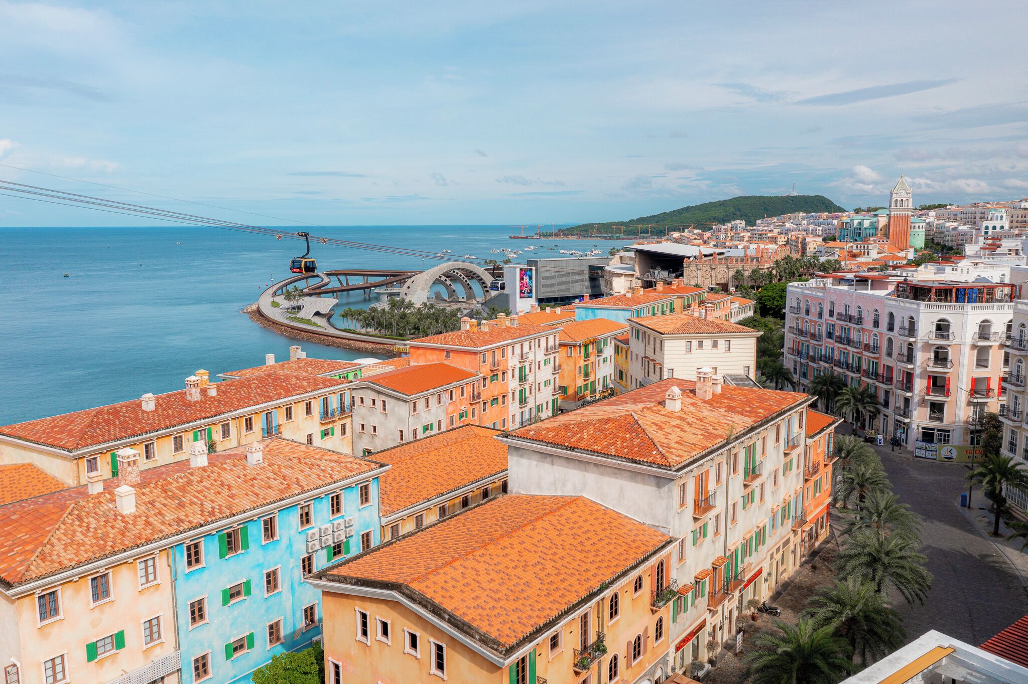 A coastal cityscape with colorful buildings, a cable car, and a view of the sea.