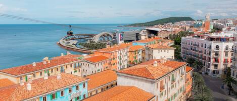 A coastal cityscape with colorful buildings, a cable car, and a view of the sea.