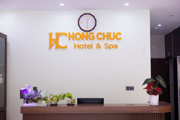 A reception desk with a clock above it, a sign for 'Hong Chuc Hotel & Spa', and a potted plant on the right. - Hong Chuc Hotel (Phu Quoc)