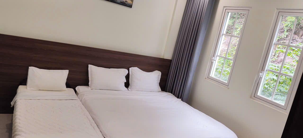 A hotel room with a large bed, a wooden headboard, and two windows with curtains.