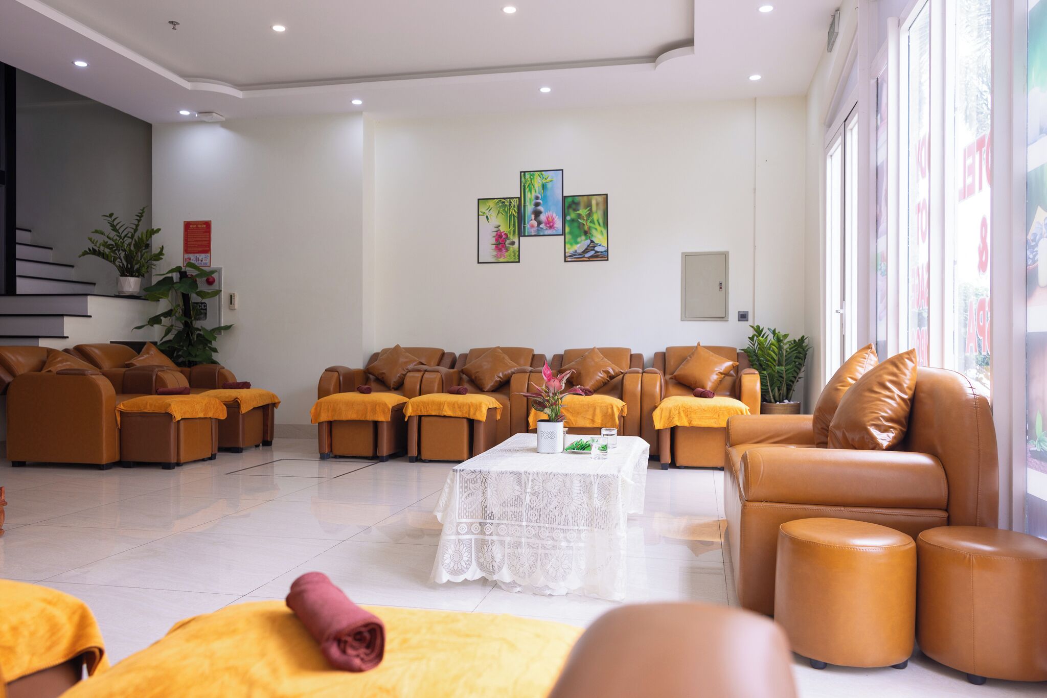 A modern lounge area with leather sofas and ottomans, a white lace table, and artwork on the wall.
