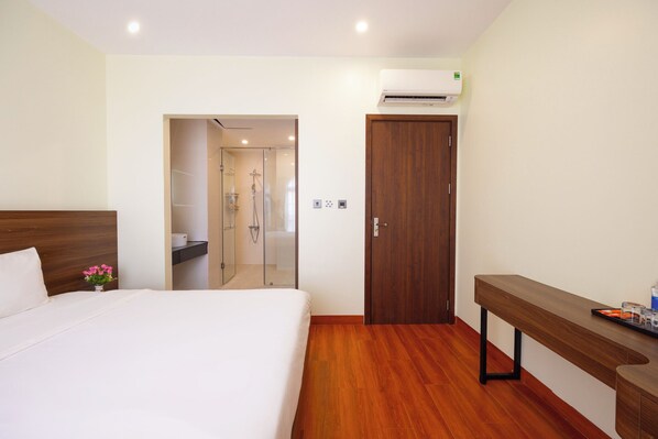 Een hotelkamer met een bed, een houten bankje, een spiegel en een deur naar een badkamer.