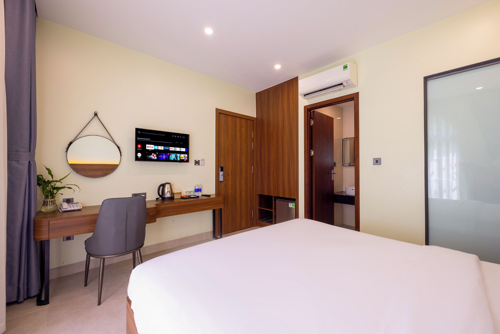 A hotel room with a bed, a desk with a chair, a TV mounted on the wall, and a wardrobe.