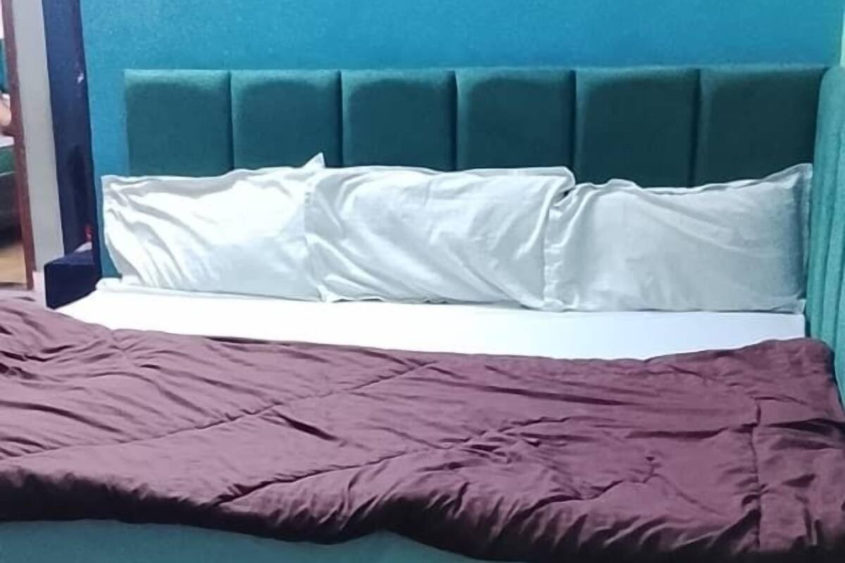 A bed with a teal headboard, white pillows, and a purple blanket.