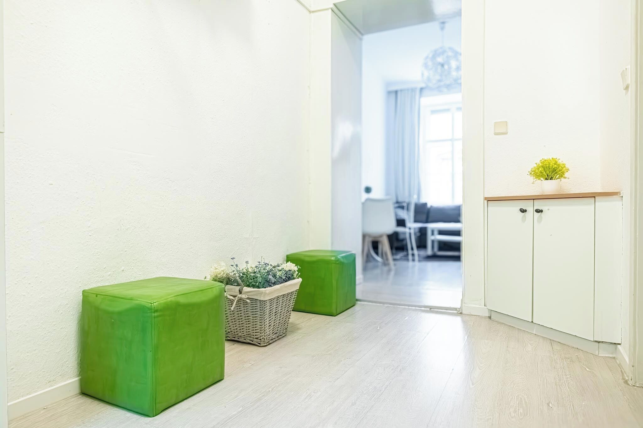 Un pasillo con asientos acolchados verdes, una cesta de mimbre con flores y un armario blanco con una pequeña planta.