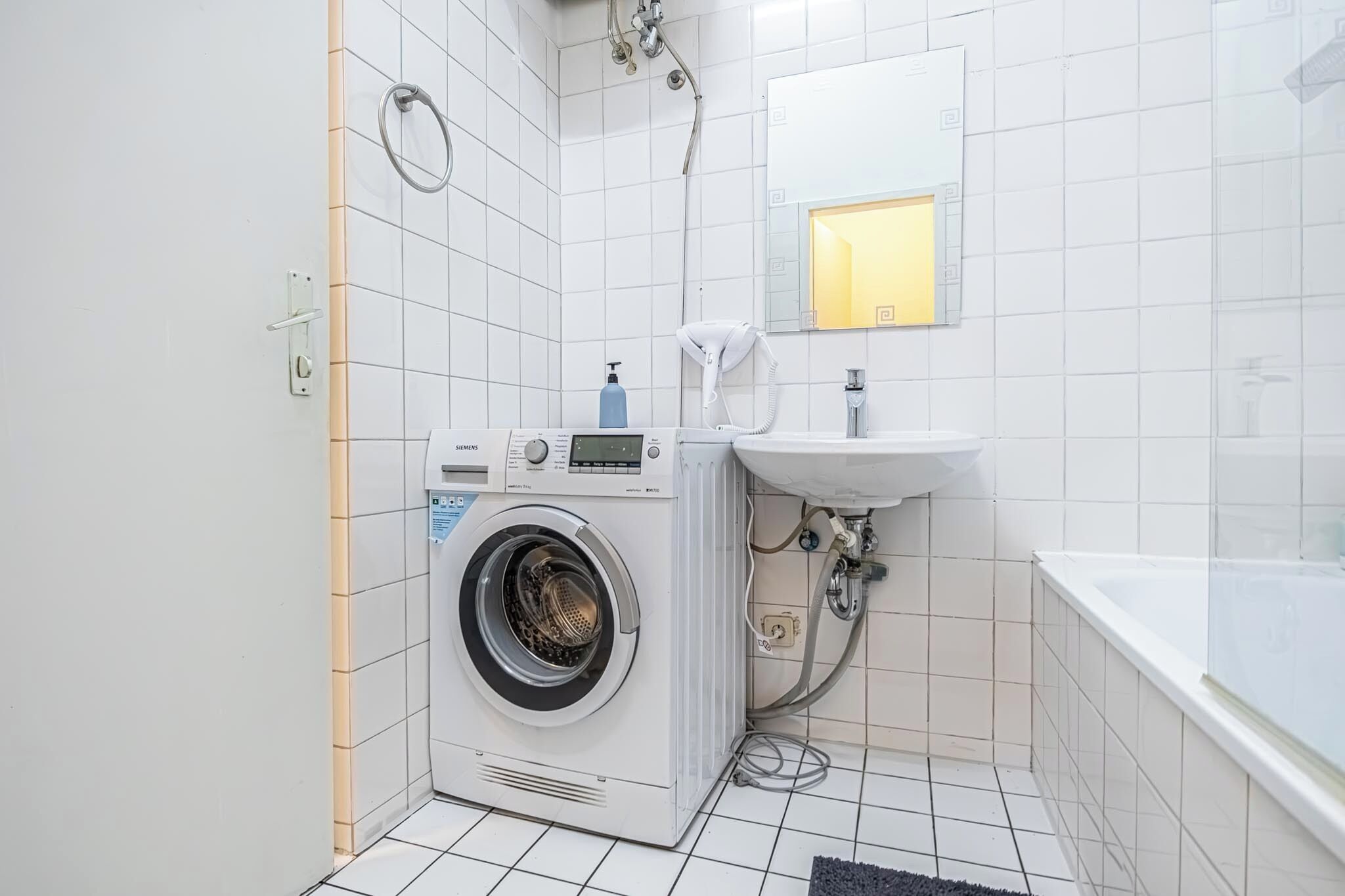 A compact bathroom with a washing machine, a sink, and a bathtub.