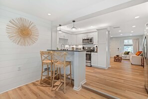 Una cocina moderna con armarios blancos, una isla central y una zona de comedor con dos sillas de madera.