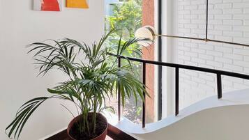 Um quarto com planta em vaso, obras de arte na parede, janela com vista para o verde e parede de tijolos brancos.