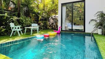 A swimming pool with clear blue water, surrounded by lush greenery and a modern building with large windows.