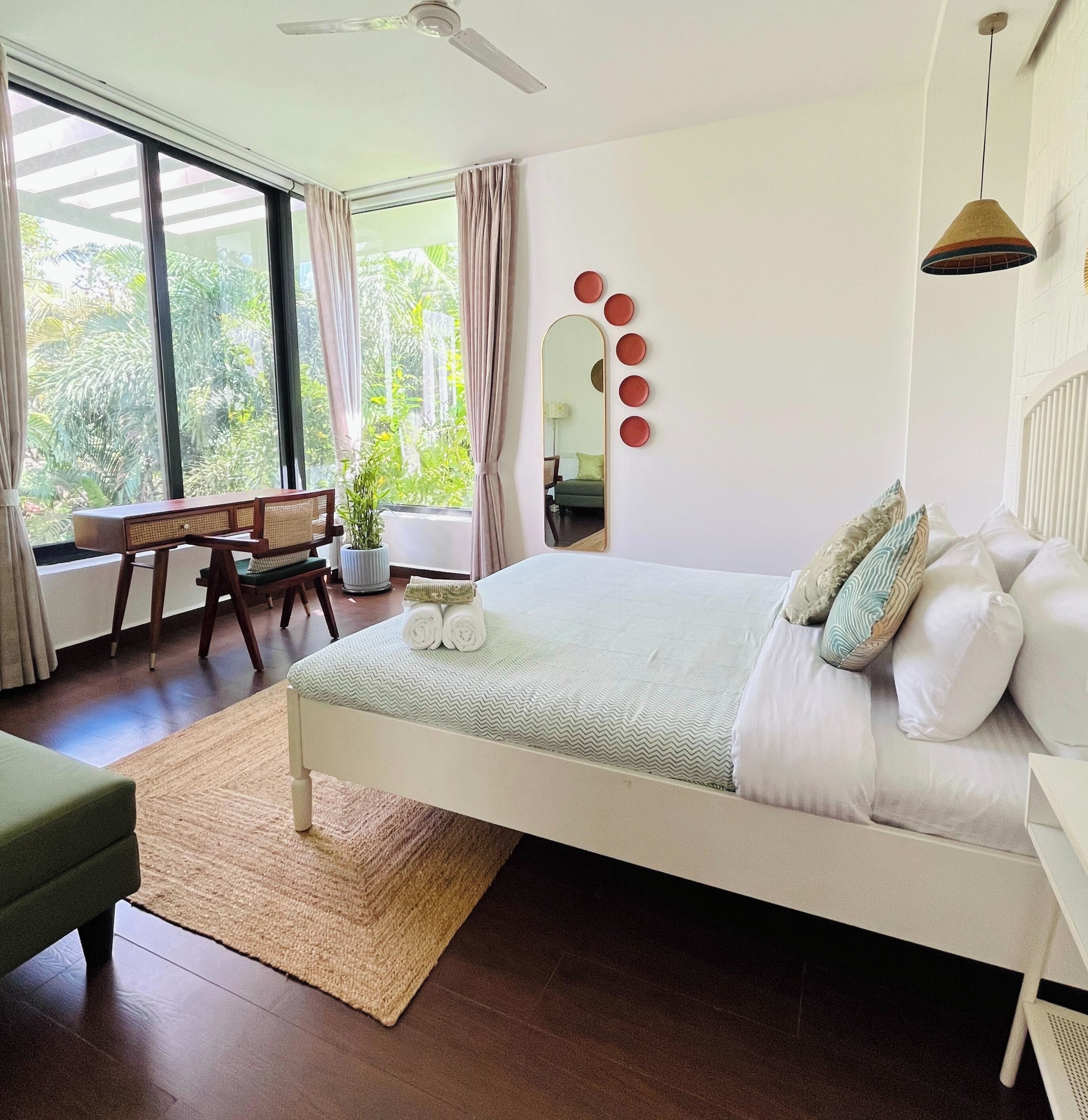Quarto com cama, escrivaninha, cadeira, espelho e vista para o verde.