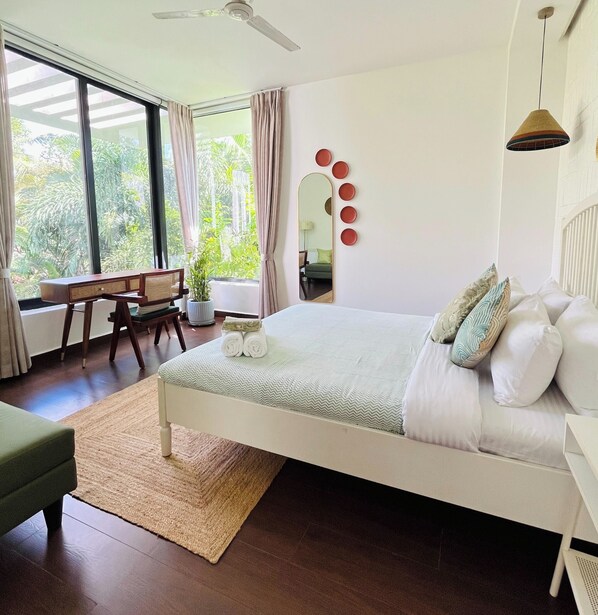 A bedroom with a bed, a desk, a chair, a mirror, and a view of greenery. - B Shore by evaddo stays (Vagator)