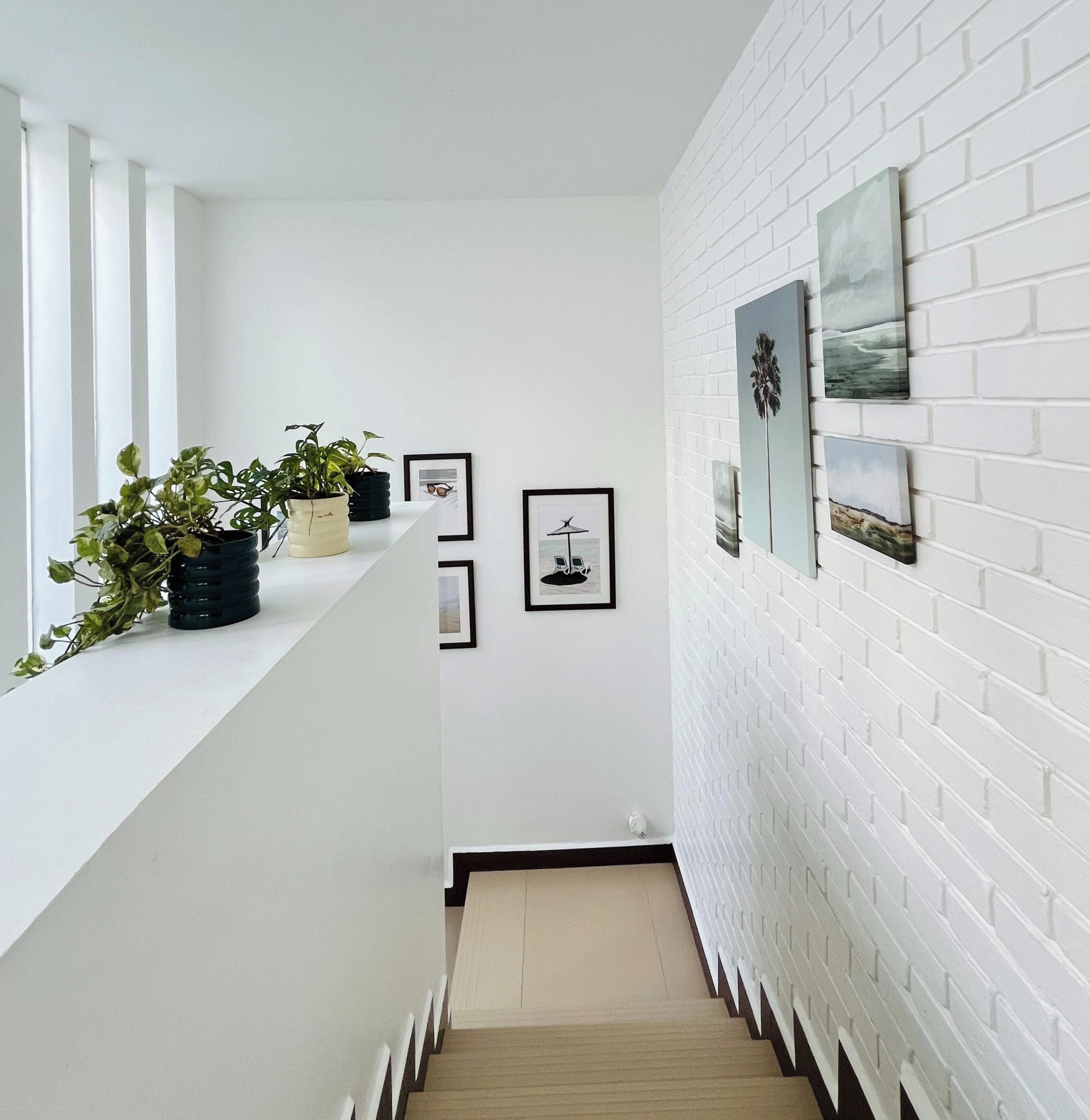 A modern interior with a white brick wall, framed artwork, and potted plants on a white ledge.