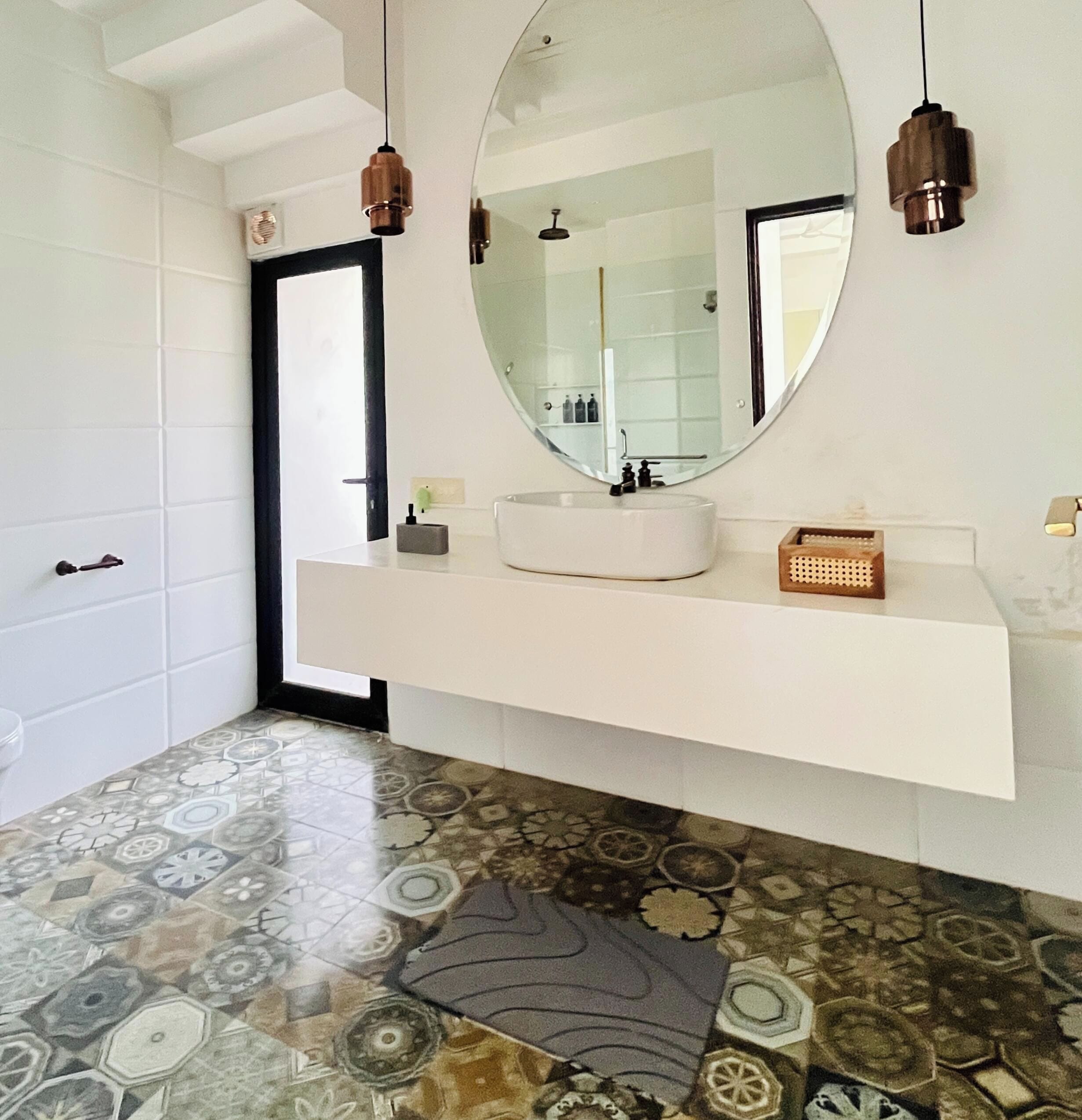 Une salle de bain moderne avec un meuble-lavabo blanc, un miroir rond et un carrelage à motifs.